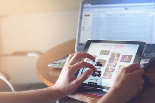 Person using a tablet, with laptop computer in the background