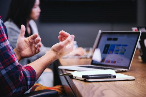 Person using their hands to gesture at a work meeting, with laptop in the background