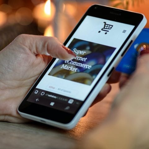a person holding a smartphone in their left hand with an ecommerce platform and a credit card in the right hand