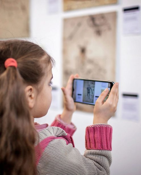 Young girl using a smartphone to take a picture of art work in a gallery.