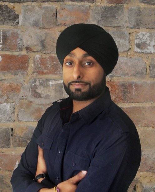 Headshot of Design Lead Kultar Ruprai with brick wall background