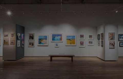 Art framed and displayed on walls at Mall Galleries. A bench is situated the middle of the room.